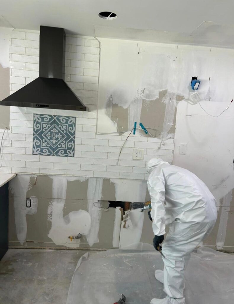 Technician in protective equipment performing controlled material removal in a contained kitchen work area in Long Beach, CA 90808.